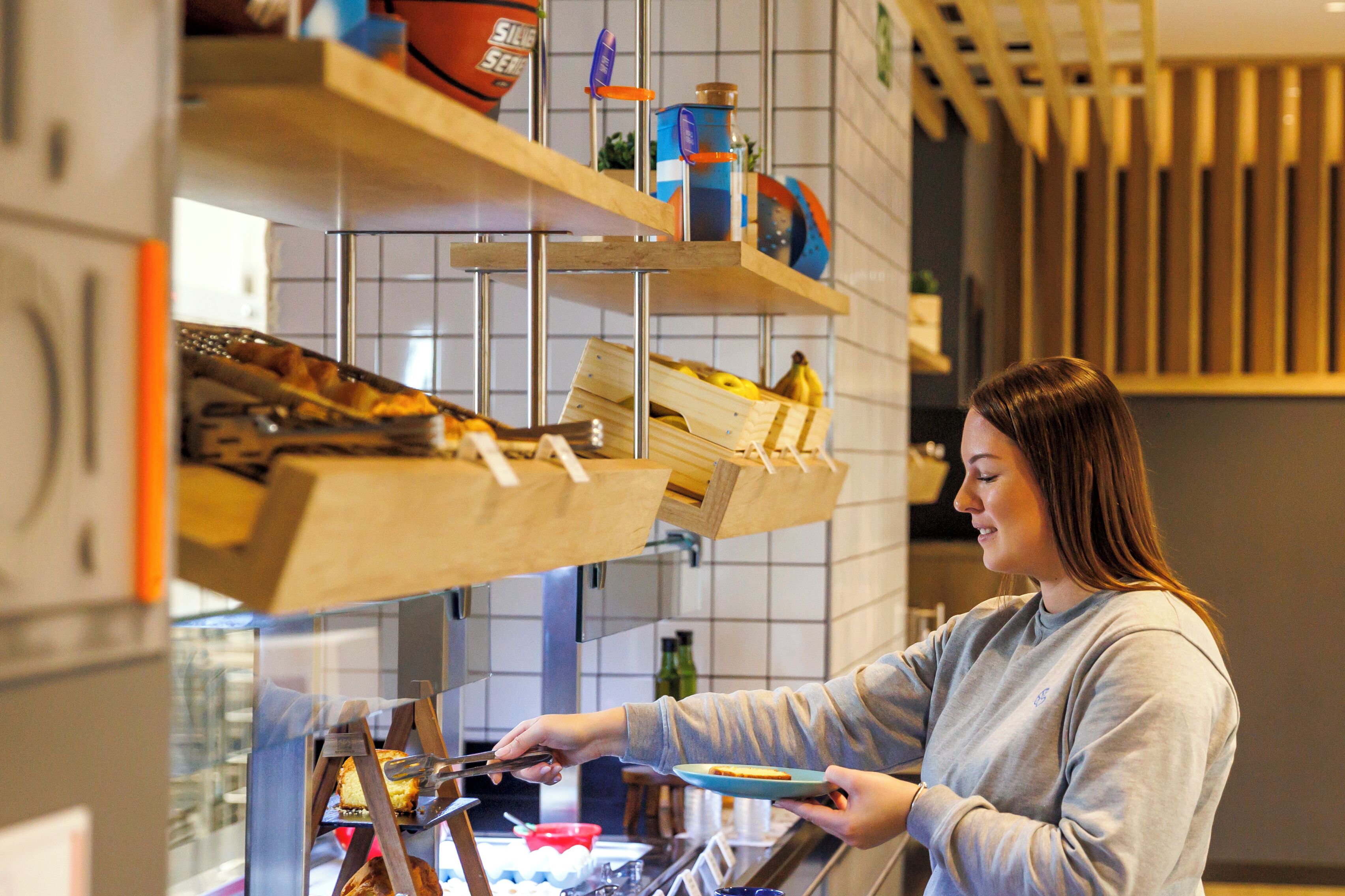 A person serving food at a counter with shelves above containing various items.