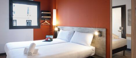 A hotel room with a large bed, a bedside table, a lamp, a window, and a mirror.