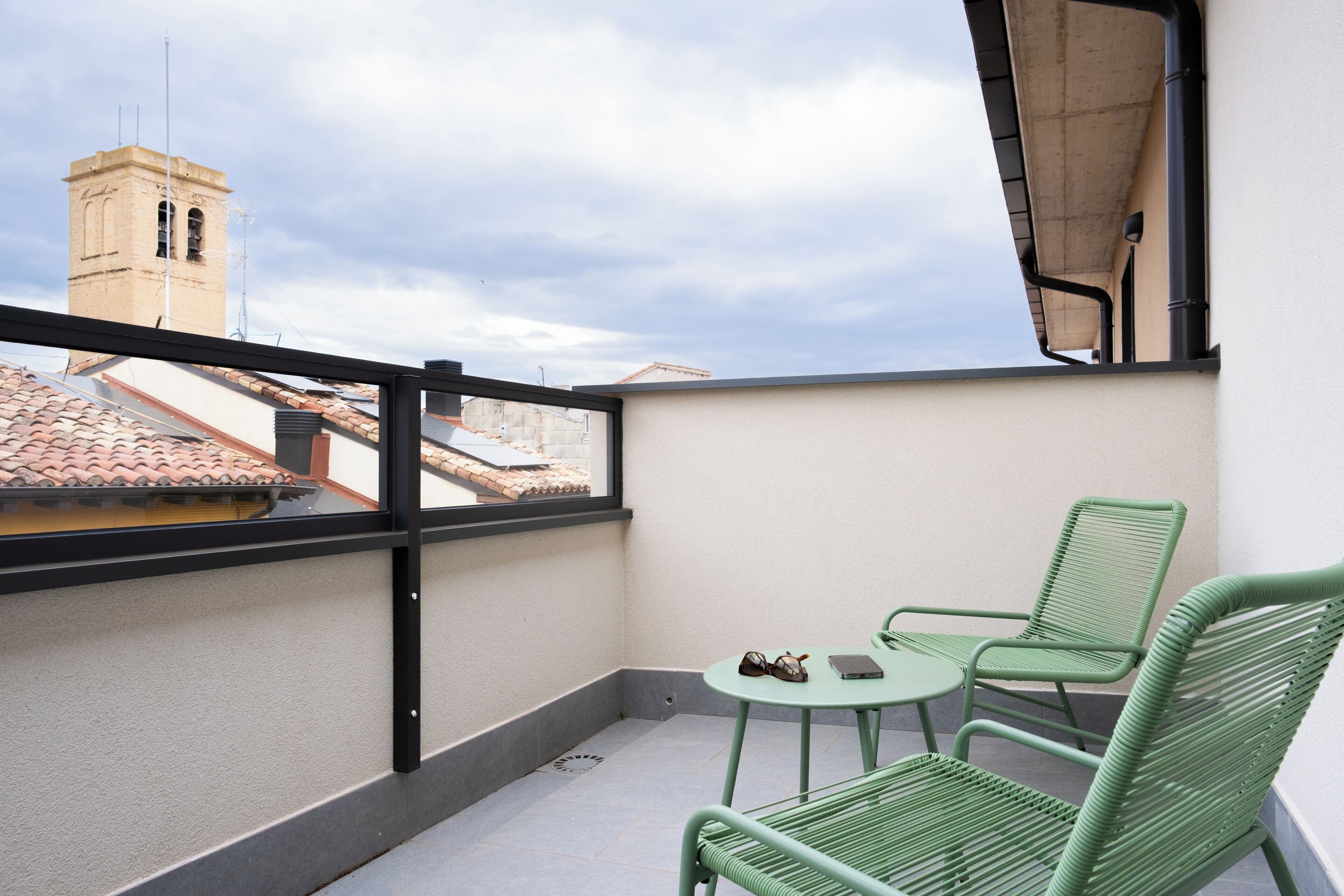 A balcony with a view of a tower, a table with chairs, and a pair of sunglasses on the table.
