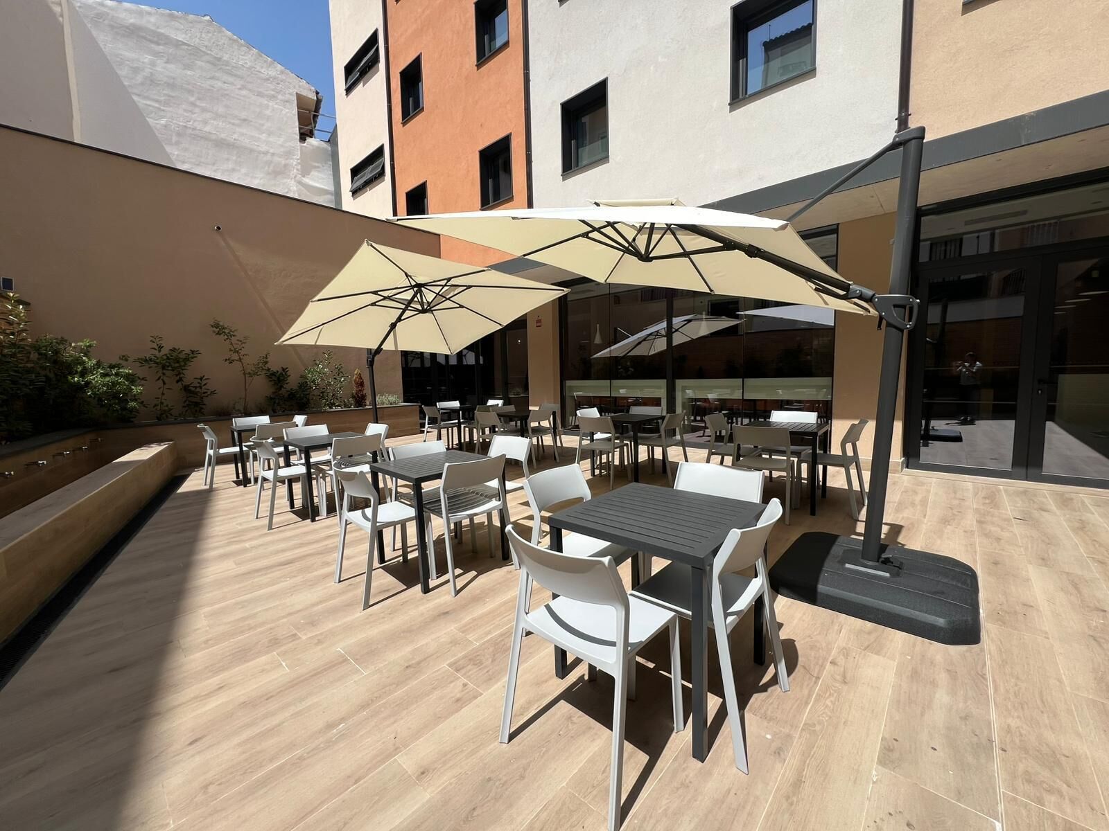 Un patio al aire libre con mesas, sillas, sombrillas y una piscina.