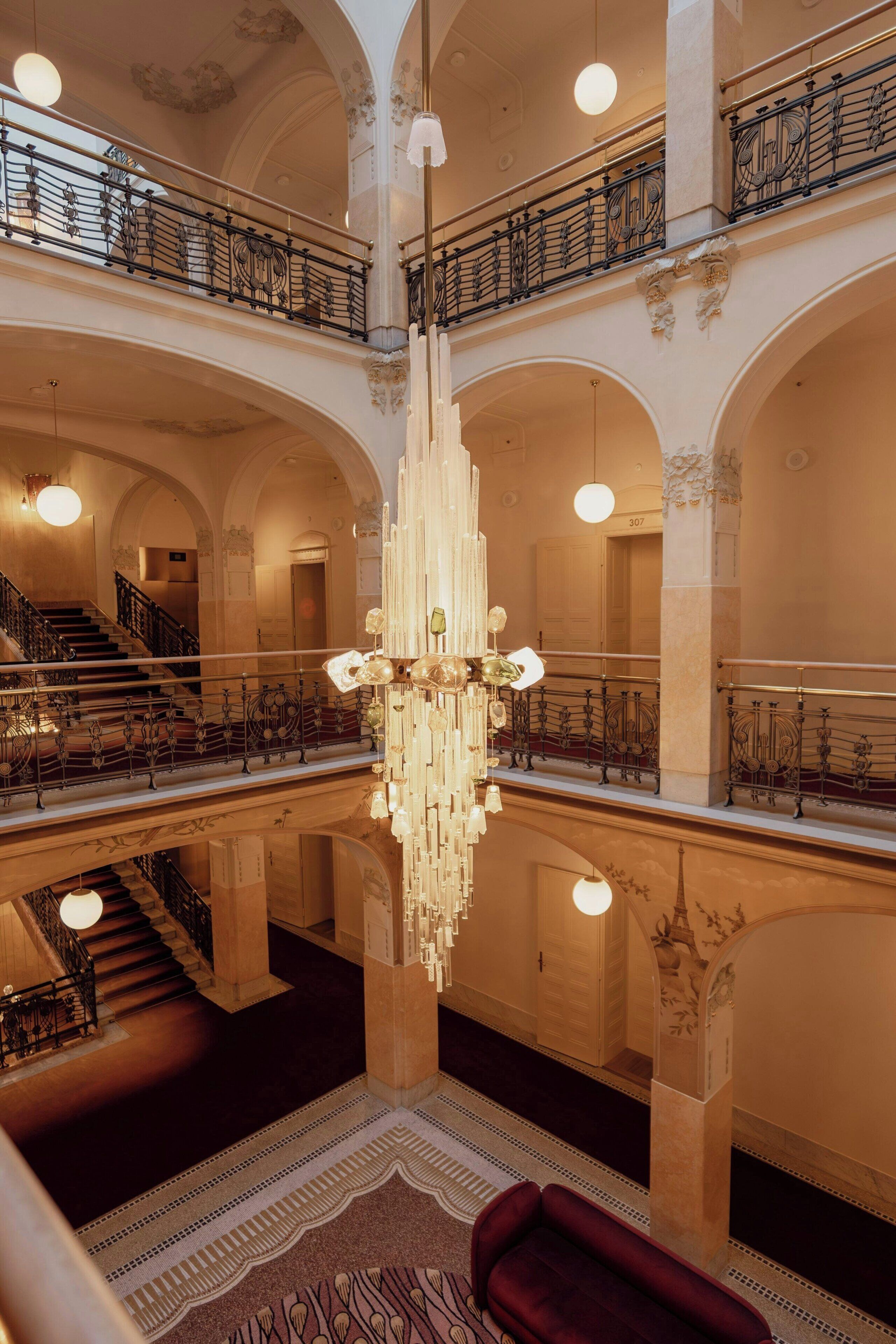 A multi-level hotel interior with ornate railings, a grand chandelier, and a staircase.