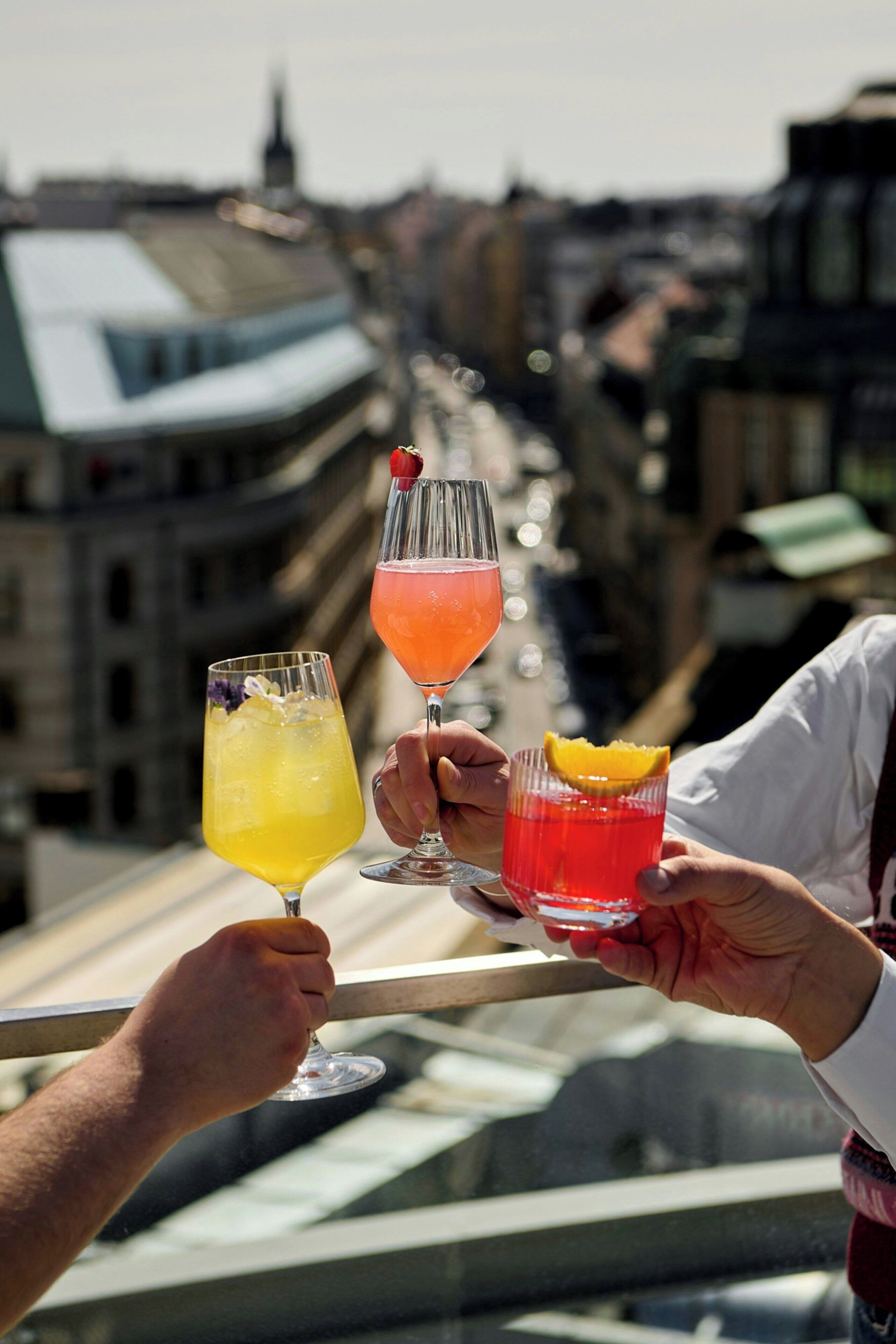 Due mani che sorreggono bicchieri da cocktail con uno skyline sullo sfondo.