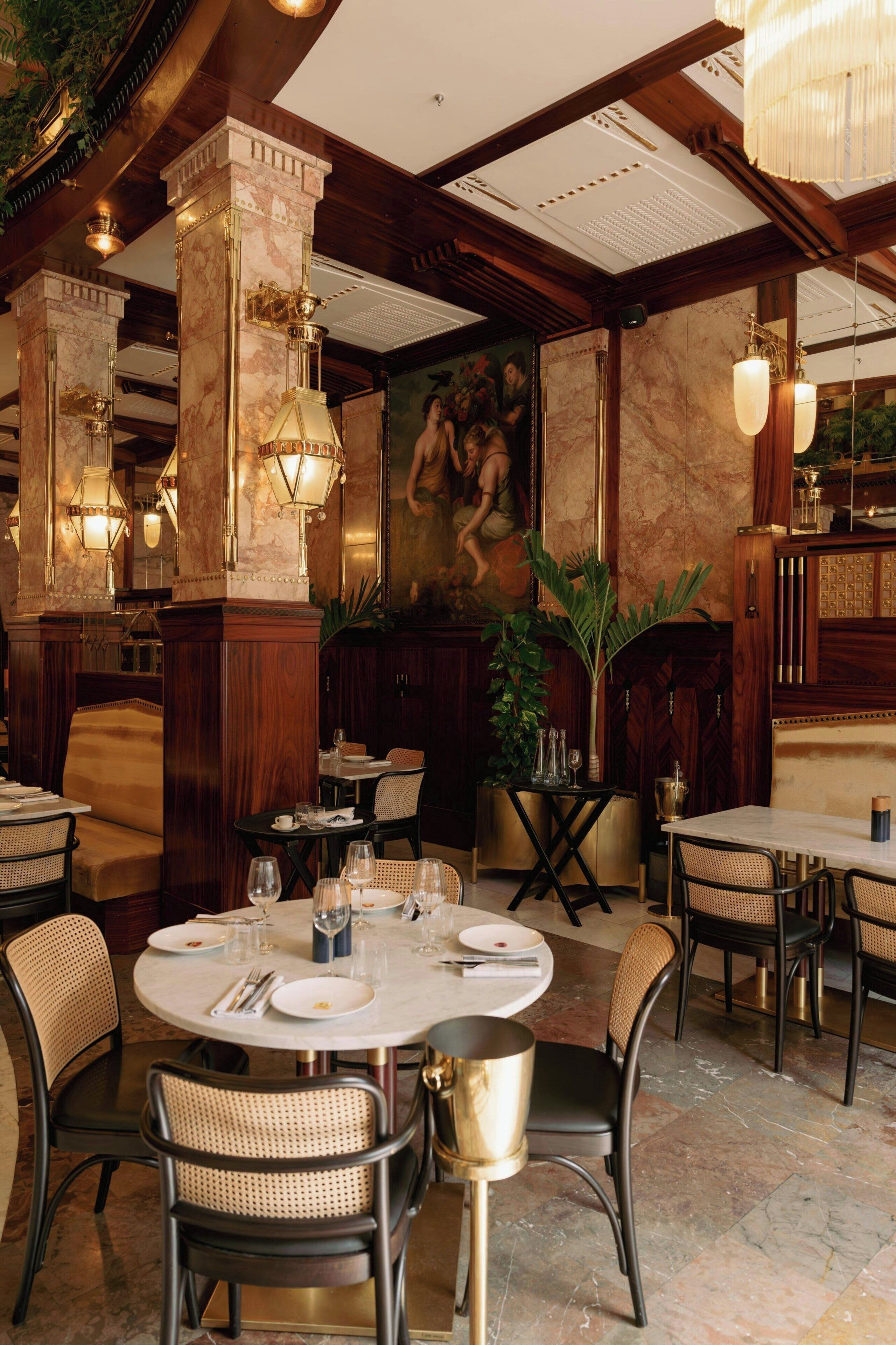 A restaurant with marble columns, round tables, wicker chairs, and pendant lighting.