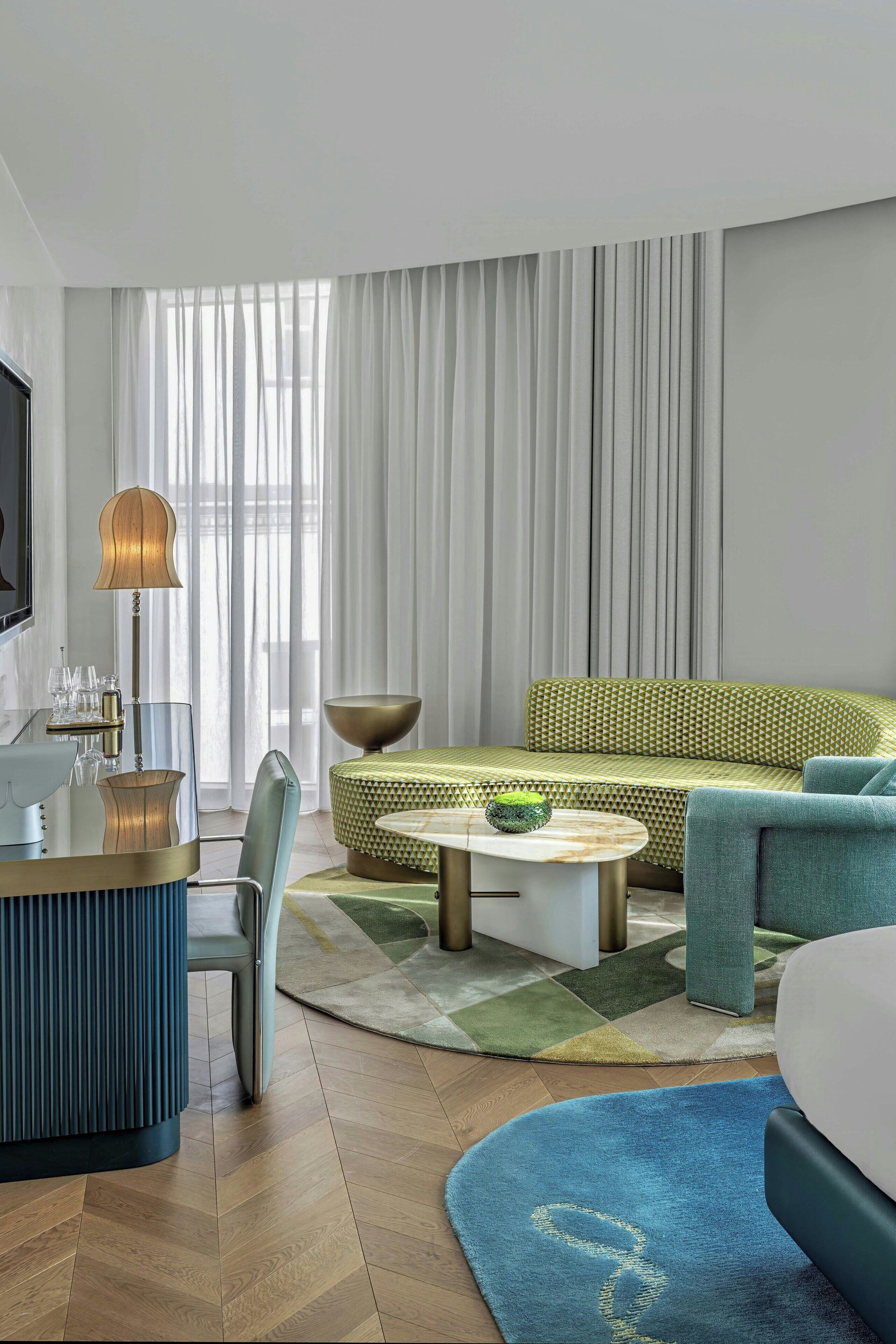 A modern hotel room with a sofa, a coffee table, a desk with a lamp, and a TV.