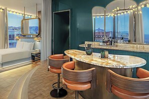 A modern hotel room with a curved bar, a large bed, and a city view.