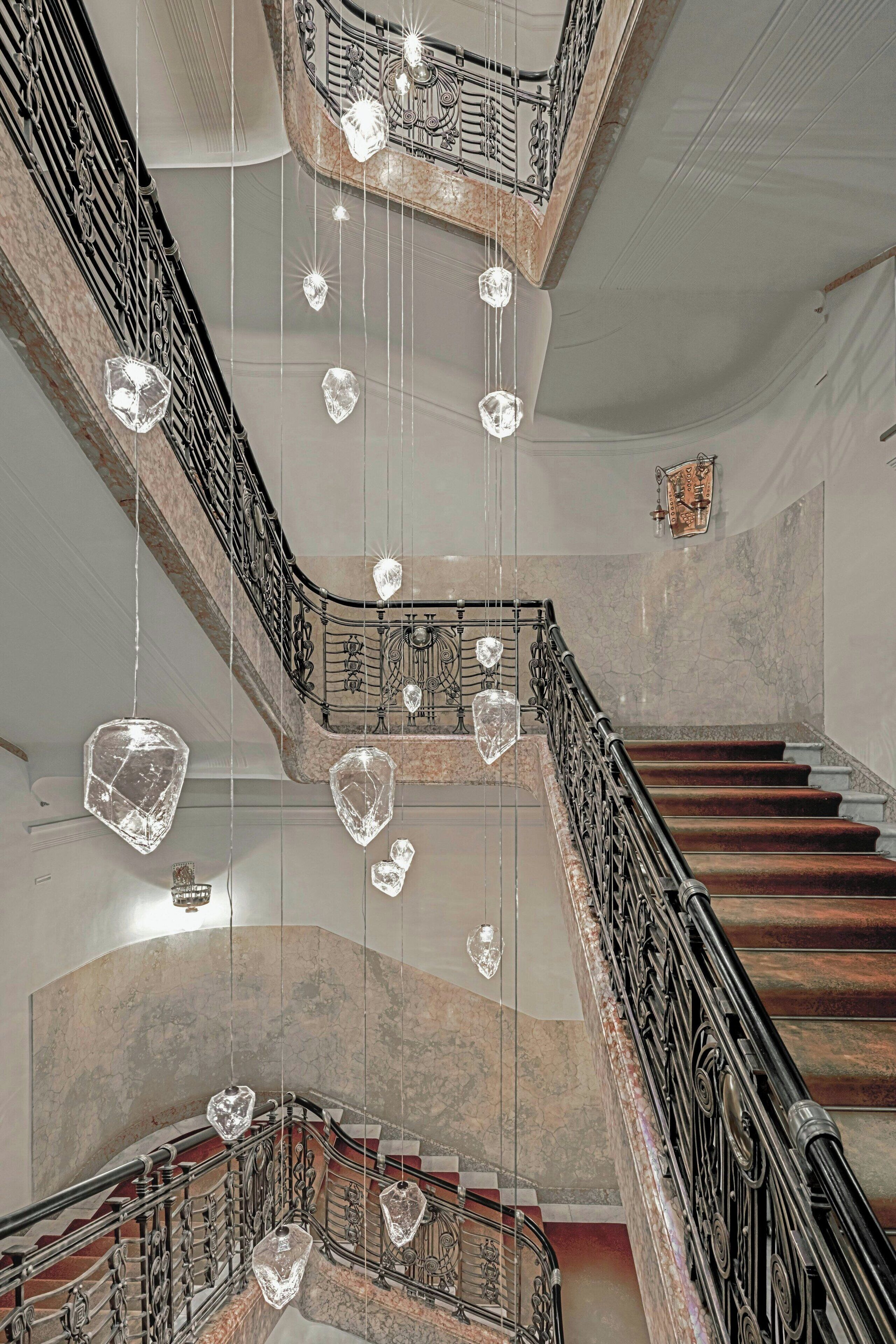 Una imponente escalera con barandillas de metal ornamentadas y lujosos candelabros de cristal.