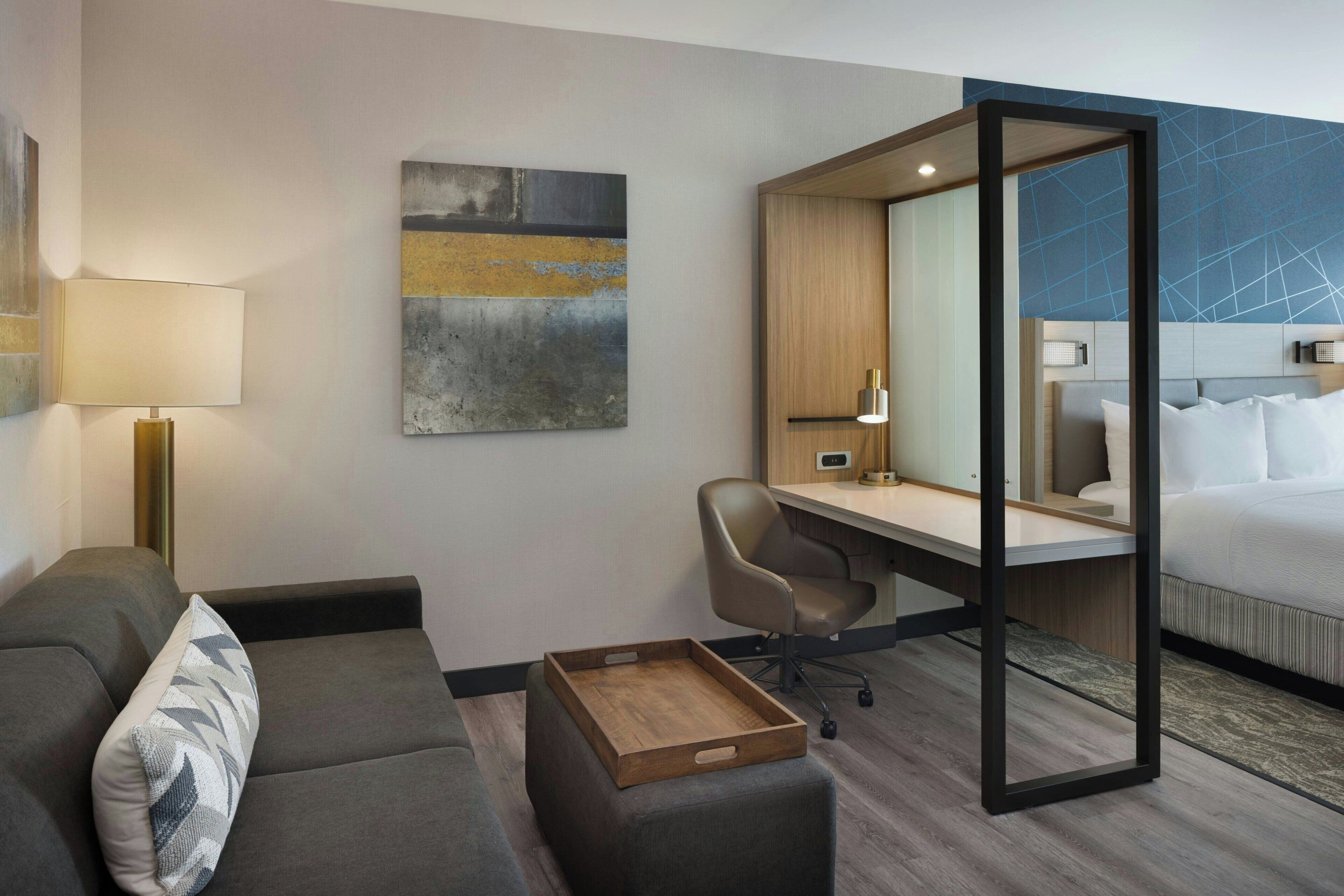 Una habitación de hotel moderna con sofá, escritorio, silla, cama y una pequeña bandeja de madera.