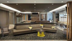 Eine moderne Hotellobby mit einer großen Eckcouch, einem runden Couchtisch und einer Sitzecke mit Sesseln und Tischen.