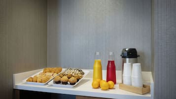 En frukostbuffé med bakverk, juice och kaffekoppar.