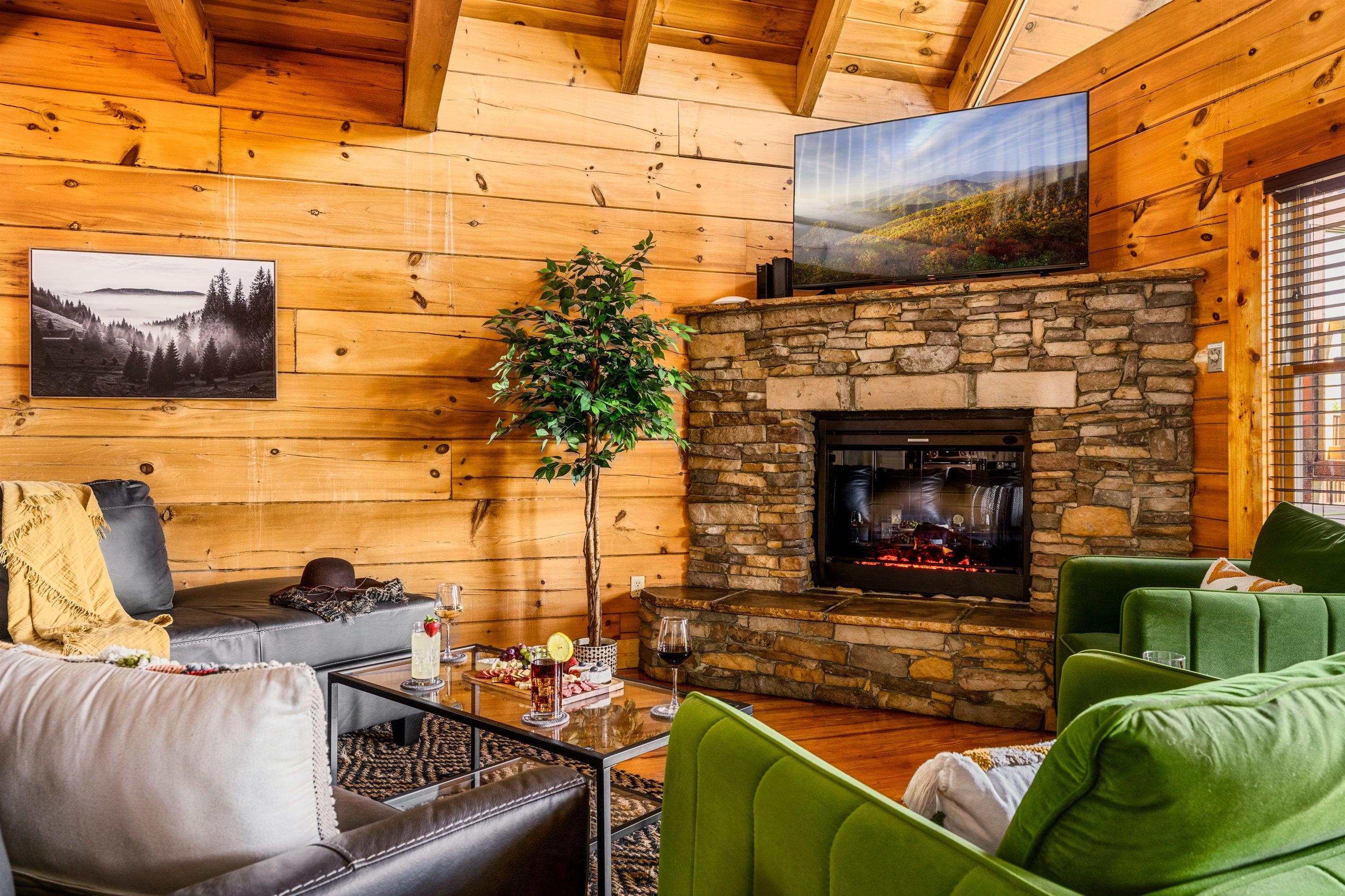 A cozy cabin interior with a stone fireplace, leather sofas, and a television mounted on the wall.