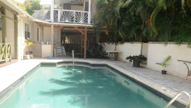 A rectangular swimming pool with a tiled edge, surrounded by a white wall and a wooden deck.