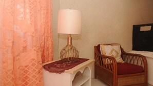 A room with a wicker chair, a small table with a lamp, and a lace curtain.