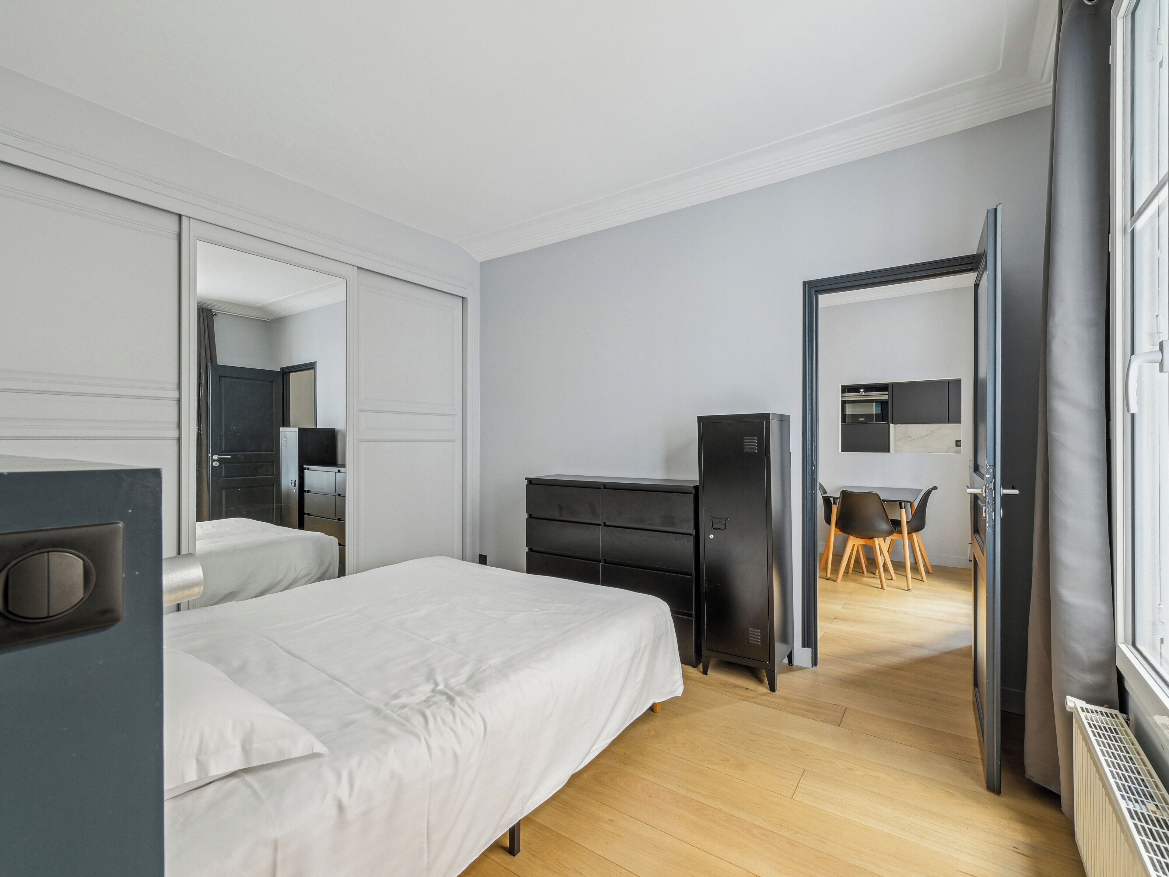 A hotel room with a bed, a desk, a chair, a wardrobe, and a mirror.