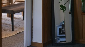 Une pièce avec un banc en bois, un miroir et une plante.