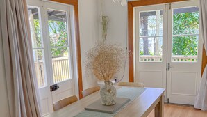 Un coin repas avec une table en bois, des chaises, un vase contenant des fleurs séchées et des luminaires suspendus.