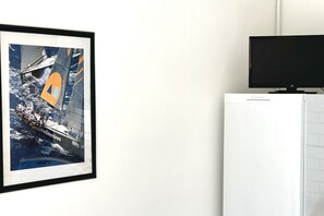 Une photographie encadrée représentant un voilier sur la mer, un téléviseur posé sur un meuble et un appareil électroménager blanc.