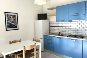 Une cuisine avec des meubles bleus, un réfrigérateur blanc, une cuisinière à gaz et un tableau encadré au mur.