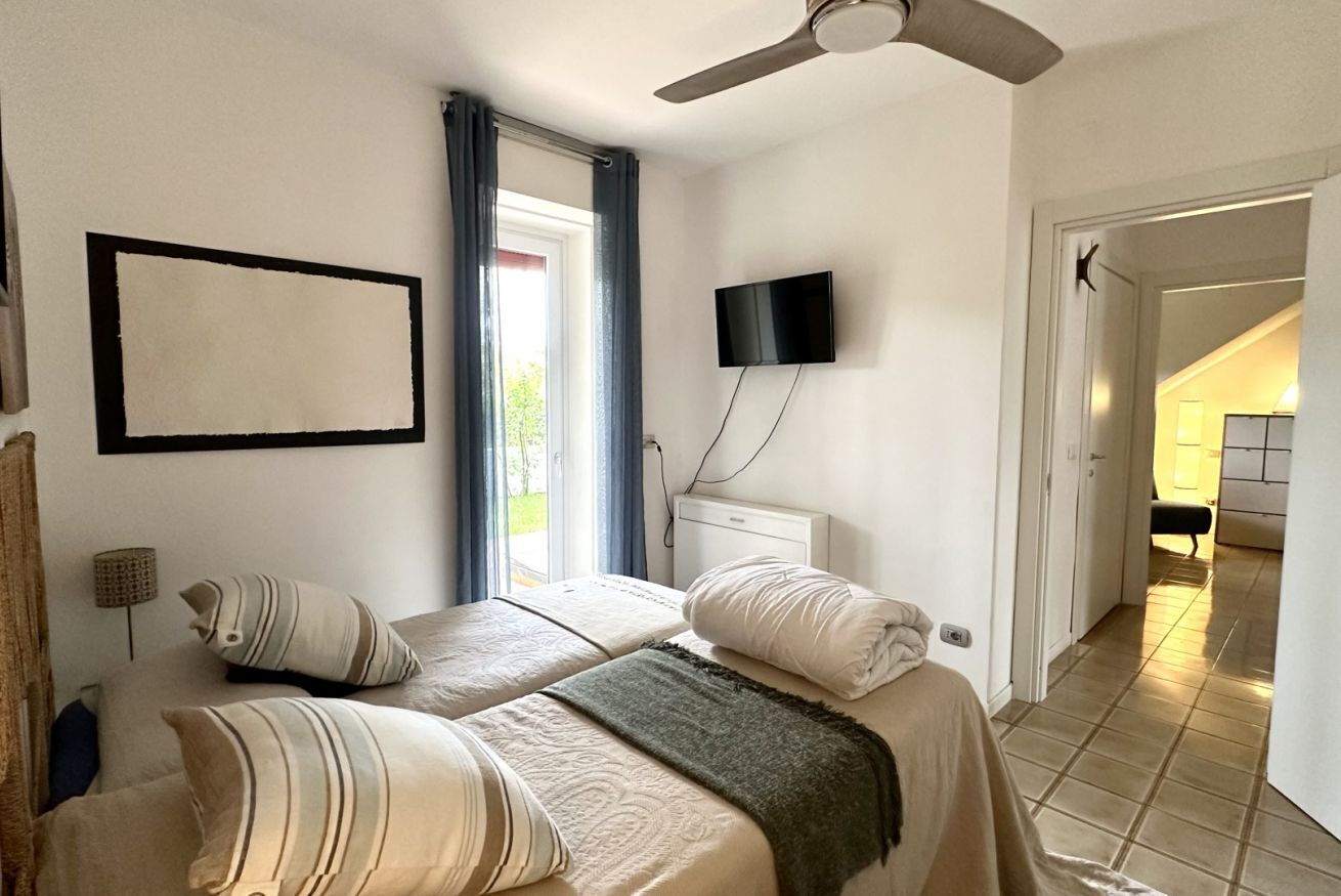 Een slaapkamer met twee bedden, een plafondventilator, een televisie en een raam met gordijnen.