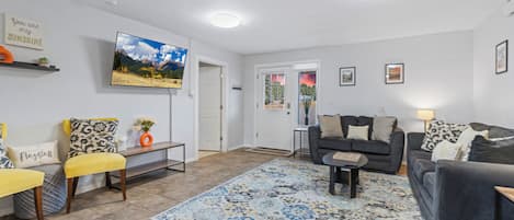 A living room with a large flat-screen TV, a sofa, a coffee table, and a patterned rug.