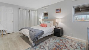 A bedroom with a bed, bedside table, nightstand, and a window with blinds. - Harmony Guest Home  (Flagstaff)