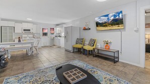 A modern living room with a large TV, a dining table, and a kitchen in the background. - Harmony Guest Home  (Flagstaff)