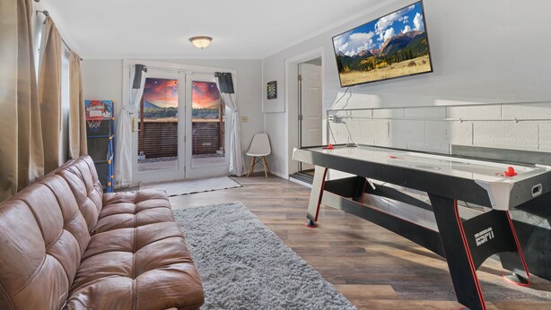 A living room with a brown leather couch, a pool table, and a TV mounted on the wall. - Harmony Guest Home  (Flagstaff)