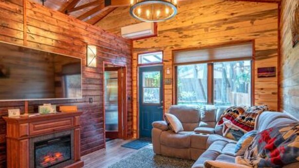 L’intérieur d’un chalet chaleureux, avec une cheminée, des murs en bois, un canapé et un lustre.