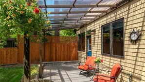 Une terrasse couverte avec deux chaises et une table, une clôture en bois et une horloge au mur.