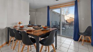 Un coin repas avec une table en bois, des chaises noires et une vue sur le jardin à travers une porte-fenêtre coulissante.