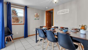 Un coin repas avec une table en bois dressée pour quatre personnes, des chaises bleues et une plante décorative.