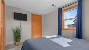 Une chambre à coucher avec un lit, un téléviseur fixé au mur, une fenêtre avec des rideaux et une porte.