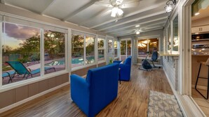 A covered patio area with large windows, blue sofas, and a ceiling fan. - Heated Pool & Hot Tub / 3 BR 2 BA / Big 360º Views (Tucson)