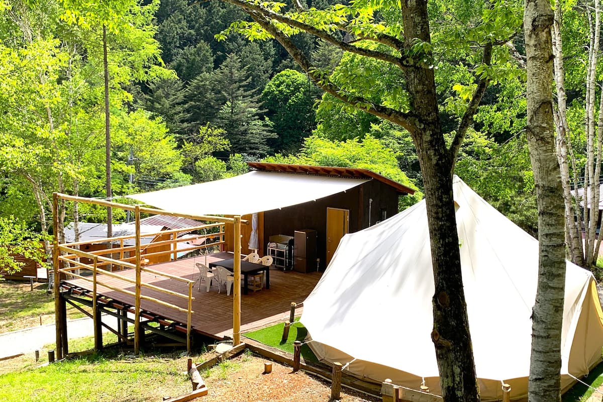 A tented accommodation with a deck, outdoor seating, and a view of the surrounding forest.