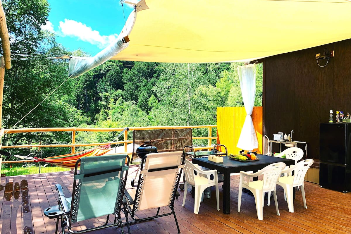 An outdoor deck with a table and chairs, a hammock, and a yellow canopy.