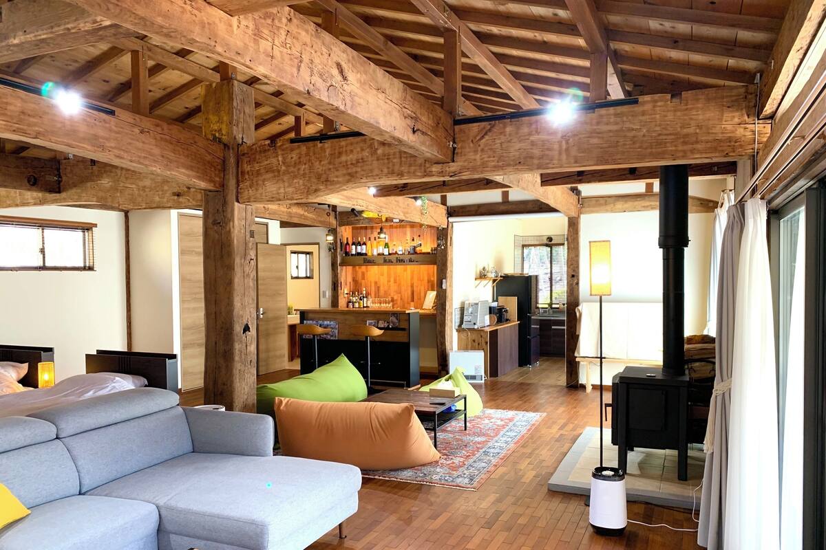 A spacious living area with a wooden ceiling, a sofa, a coffee table, and a bar area with bottles and a coffee machine.