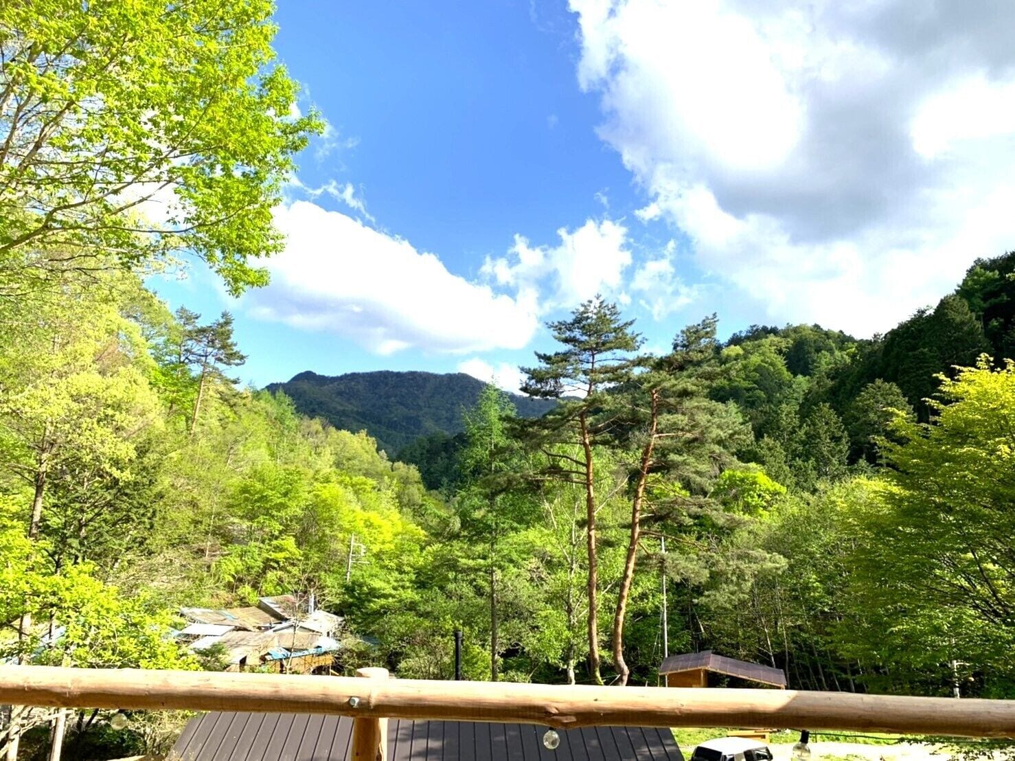 A forested area with a mountain in the background, a wooden deck, and a small building with a sloped roof.