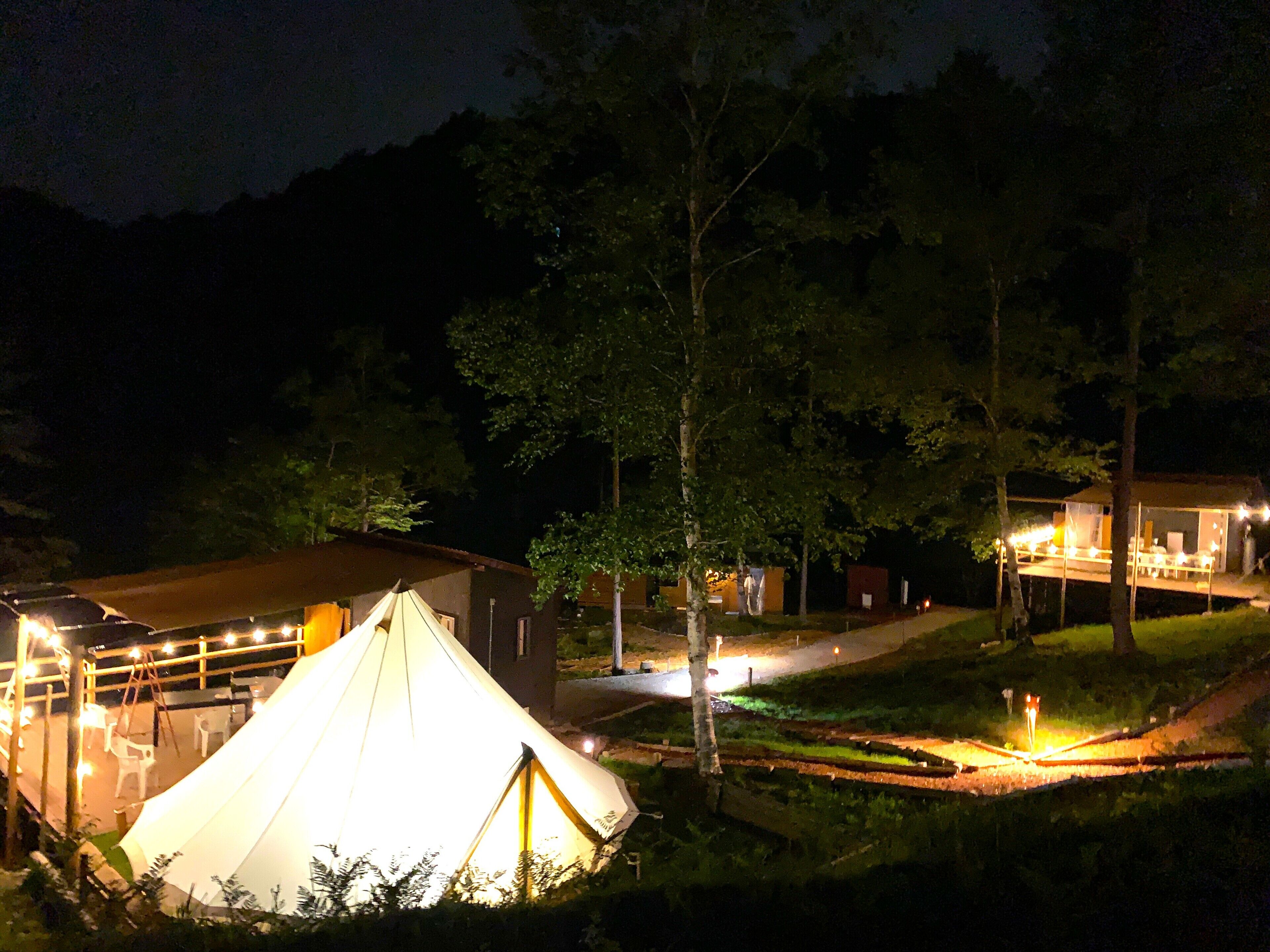 A tented accommodation with a covered outdoor seating area and a pathway leading to a building.