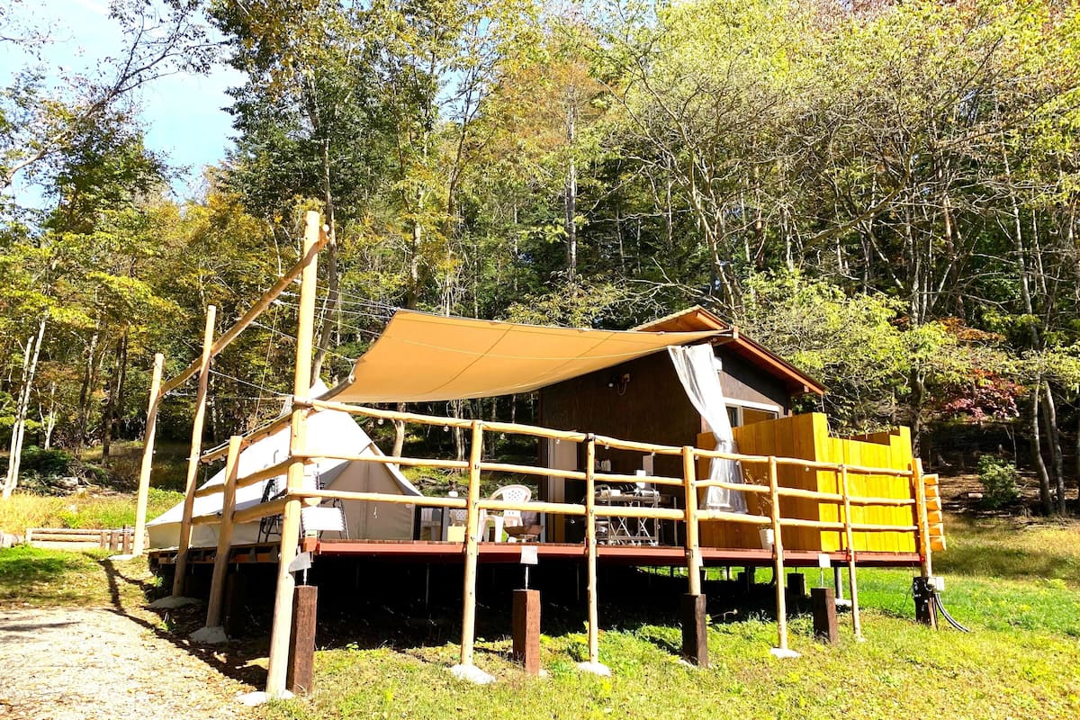 A rustic wooden cabin with a covered deck, surrounded by trees.