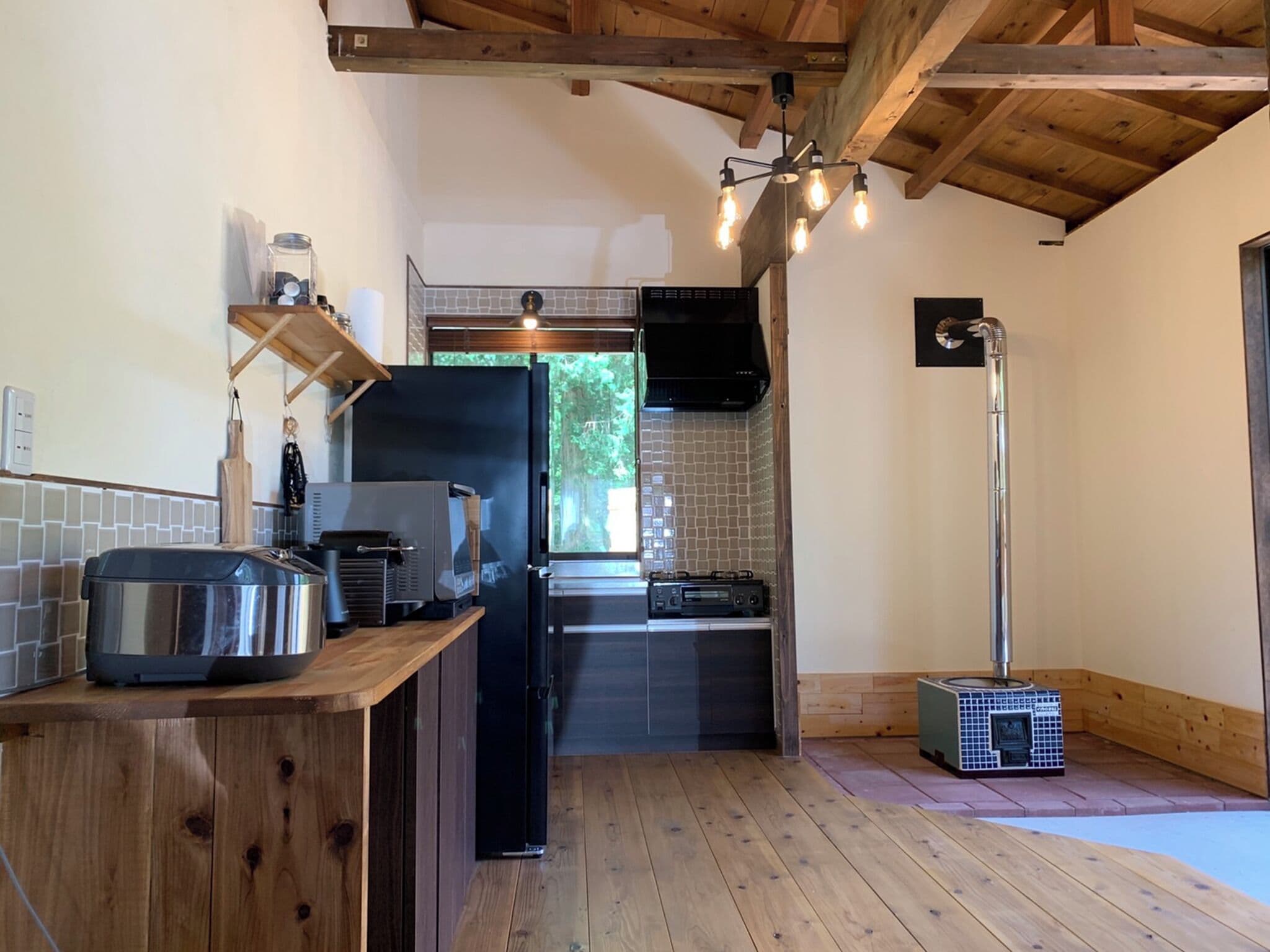 A compact kitchen with a wooden countertop, a black refrigerator, a built-in oven, and a window with a view of greenery.