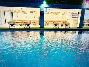 Una piscina con sillones de descanso y mesas, rodeada por un edificio de diseño moderno.