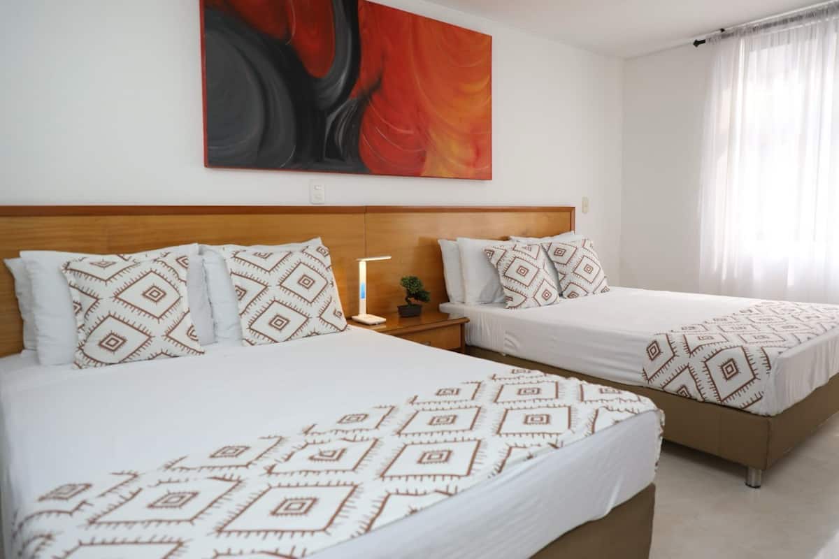 A hotel room with two beds, each with patterned bedding and pillows, a bedside table with a lamp, and a large abstract painting on the wall.