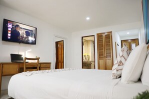 Un dormitorio con una cama, un escritorio con una computadora portátil, un televisor montado en la pared y un armario con puertas correderas.
