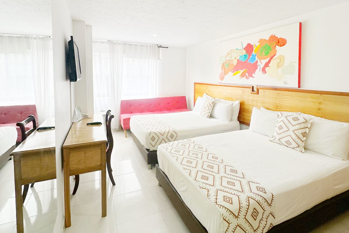 A hotel room with two beds, a desk, a chair, and a sofa.