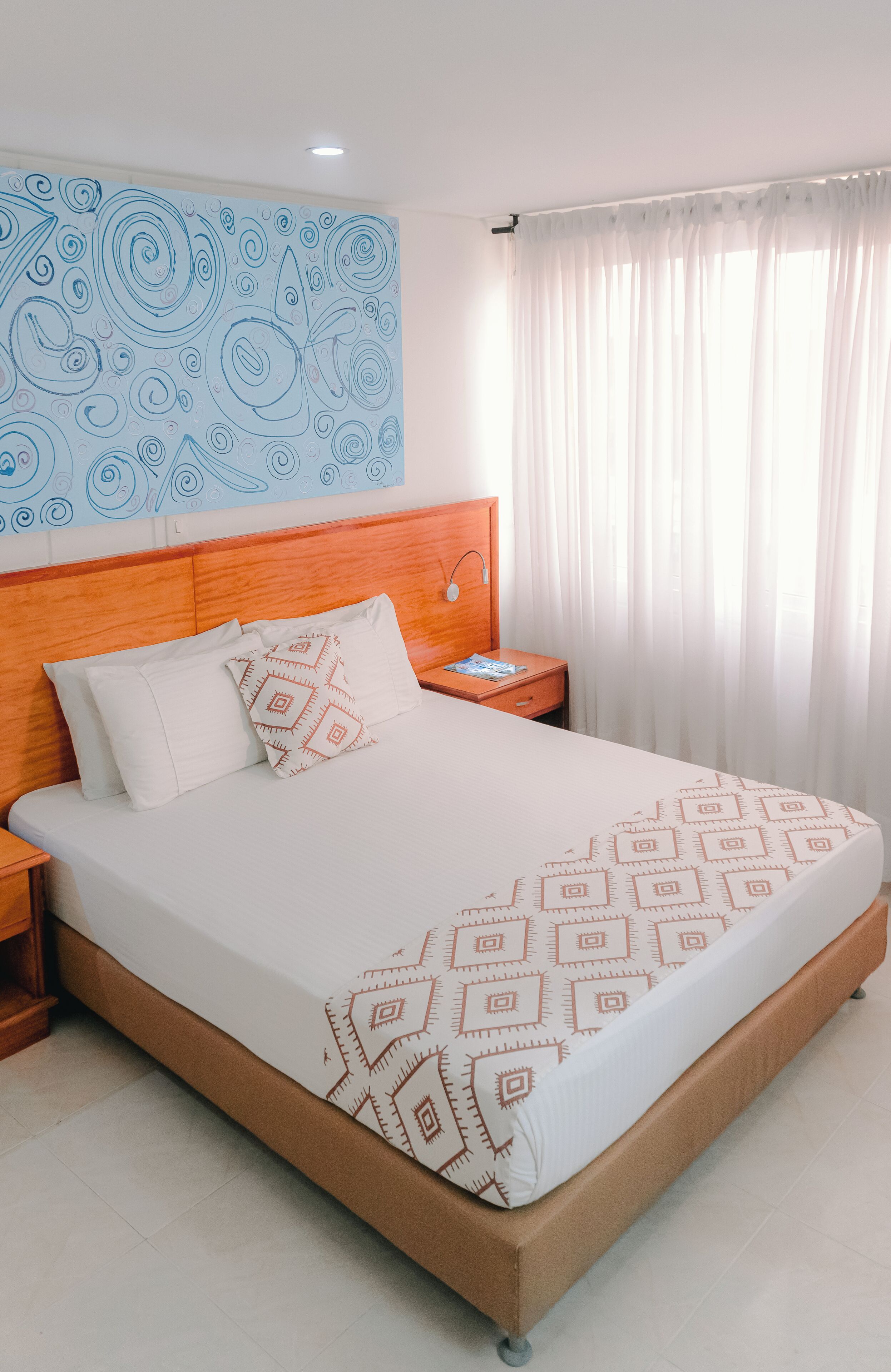Habitación de hotel con una cama grande, cabecera de madera, ropa de cama blanca y una obra de arte abstracto azul en la pared.