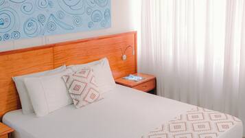 Habitación de hotel con una cama grande, cabecera de madera, ropa de cama blanca y una obra de arte abstracto azul en la pared.