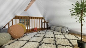 Una habitación cálida en el ático, con techo inclinado, una escalera de madera y una planta en maceta.