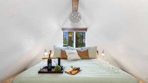 Un dormitorio acogedor y bien iluminado con una cama grande, una mesita de noche con lámpara y una ventana con vistas a árboles.