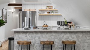 Una cocina moderna con una isla central, electrodomésticos de acero inoxidable, taburetes de bar de madera y un salpicadero geométrico.