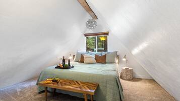 A cozy attic bedroom with a sloped ceiling, a bed with a green quilt, a small round side table, and a wooden bench.