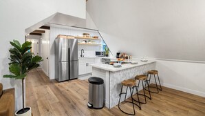 Una cocina moderna con armarios blancos, electrodomésticos de acero inoxidable y una isla central con taburetes.